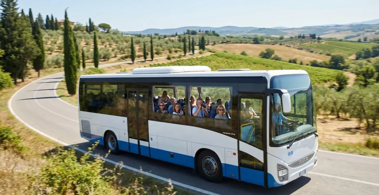 Modern tourism bus with large windows traveling along a cypress-lined road through rolling Tuscan hills